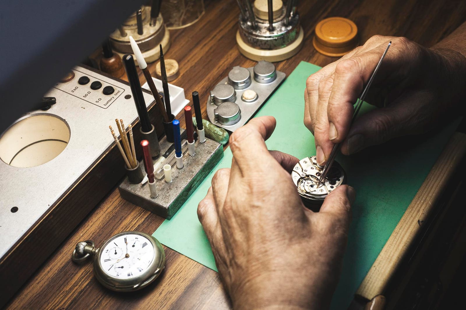 Banco da orologiaio con un orologio da tasca antico, cacciaviti e uno strumento di collaudo d'epoca